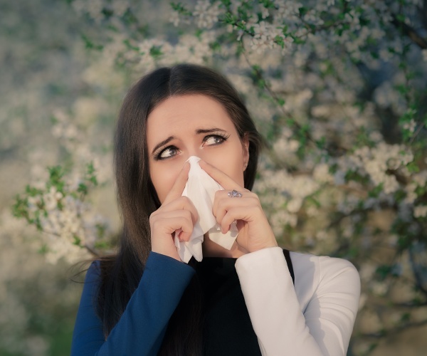 woman outside in spring next to flowering trees blowing nose and eyes watering