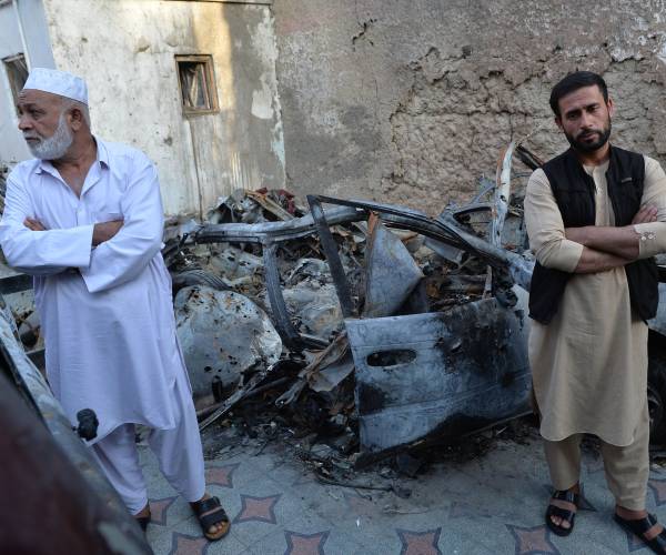 two men stand in front of the burned out vehicle