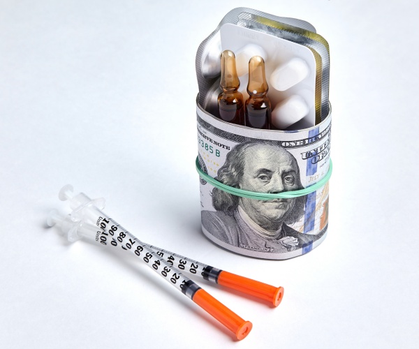 syringes, insulin, pills in a glass with $100 bills