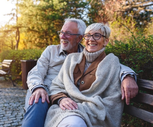 older man and woman smiling while sitting together on park bench