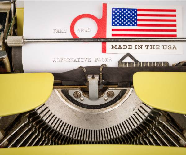 a typewriter with fake news typed on paper and an american flag sticker