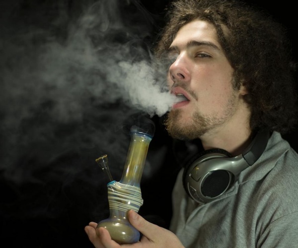 young adult male with beard smoking marijuana from a bong