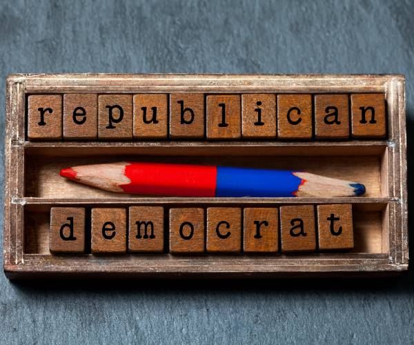 block letters spelling out republican and democrat inside a wooden box with a double sided blue and red pencil