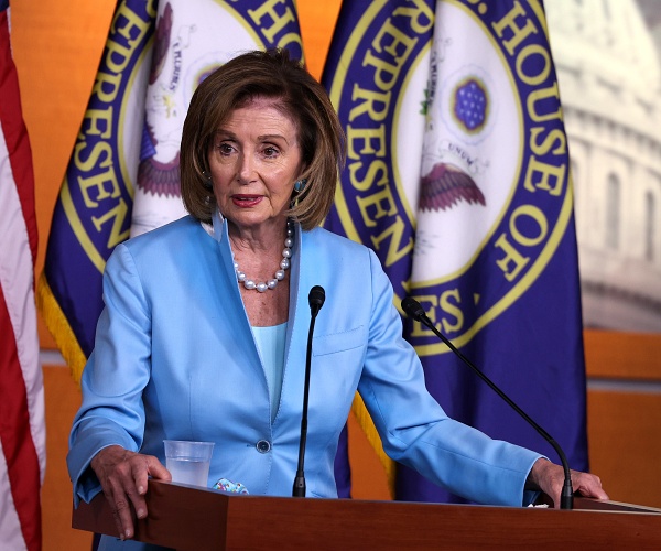 nancy pelosi rests hands on podium and speaks into mic