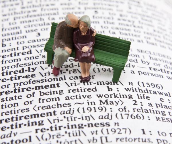 miniature of a retired couple sitting on a bench with the definition of retirement in a dictionary beneath them