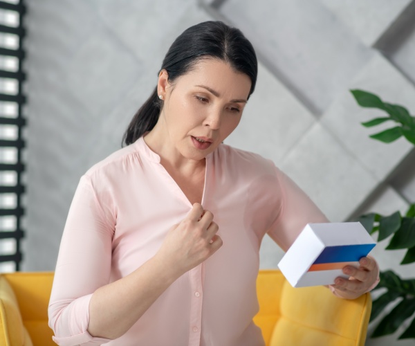 woman having a hot flash and holding a box of hormone replacement therapy