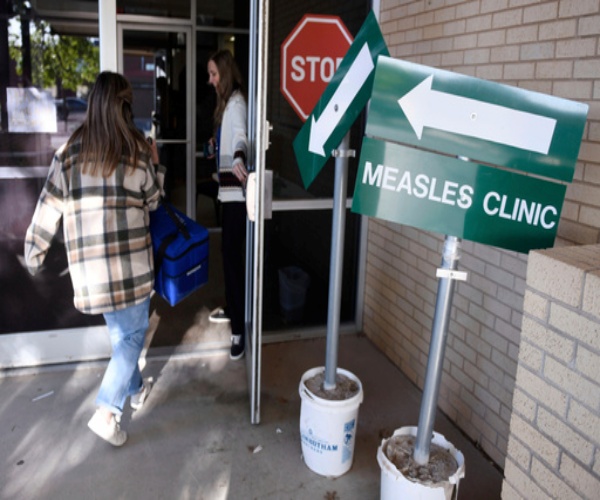 person walking into a building with a sign outside that says "Measles Clinic"