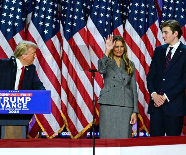 donald trump looks at melania and barron trump on stage in front of a row of american flags