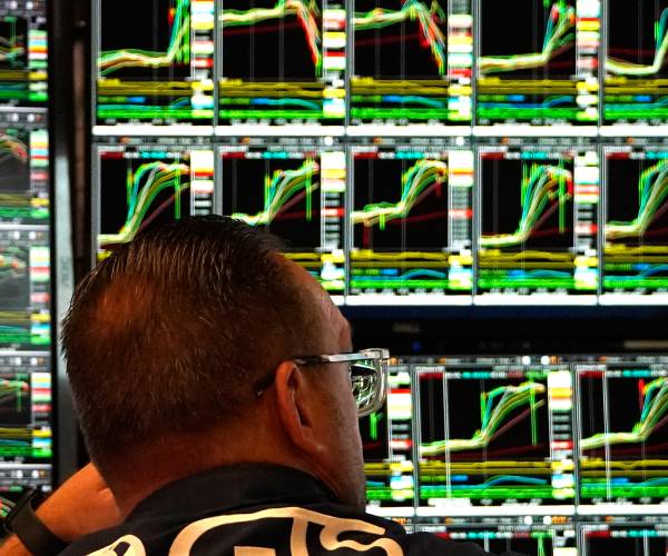 a man sits in front of screens showing stocks up