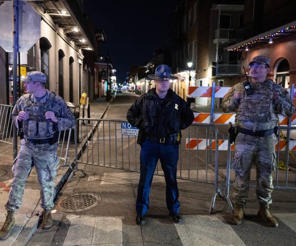 two national guard members and one police officer stand in  front of a barricade on a street