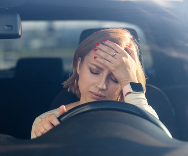 woman suffering fatigue holding head while driving car