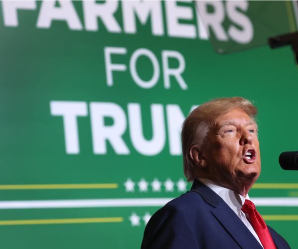 donald trump speaking in font of a sign reading farmers for trump