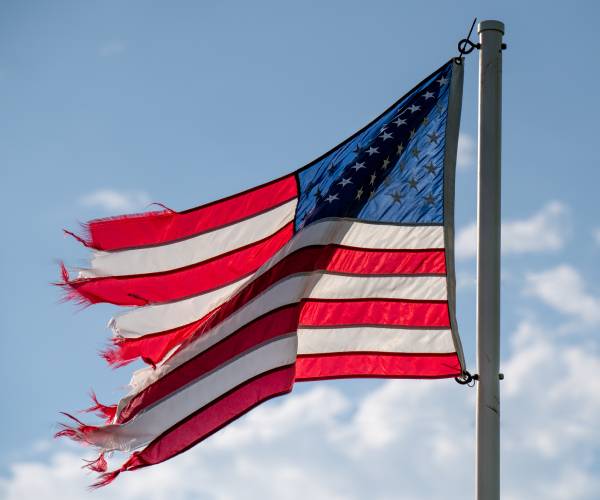 a tattered american flag waves on a flagpole against a cloudy sky