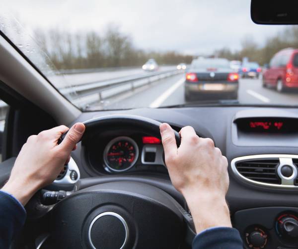 hands on a steering wheel looking out the windshield into traffic on a highway