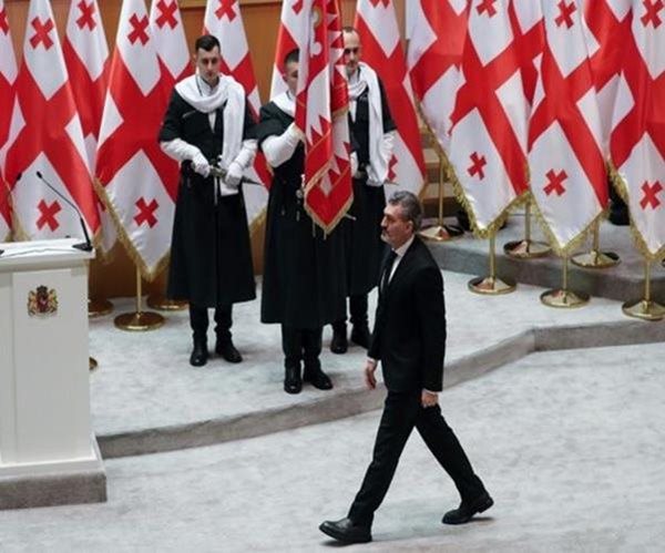 man walks in front of georgian flags