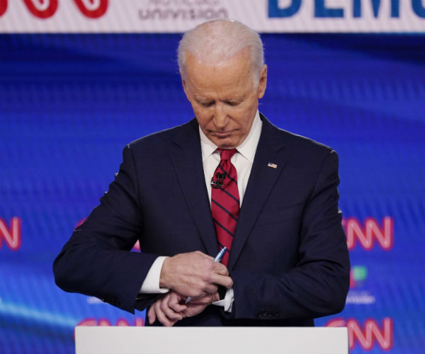 joe biden is shown on the debate stage checking his watch