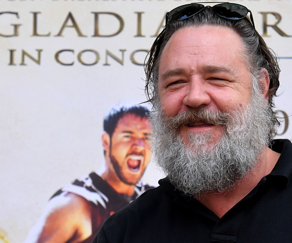 russell crowe smiling in front of a poster for the movie gladiator