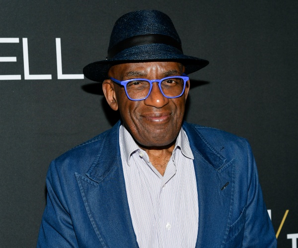 roker in a blue blazer, blue framed glasses and a hat