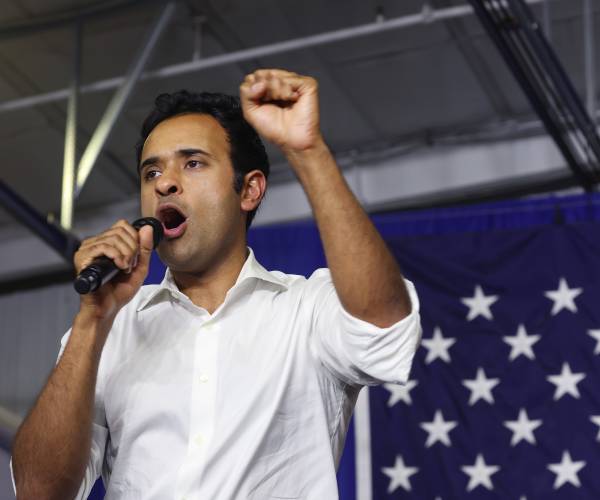 vivek ramaswamy raises a fist and holds a microphone while speaking