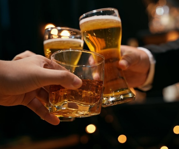 people in a bar clinking together glasses of beer and liquor