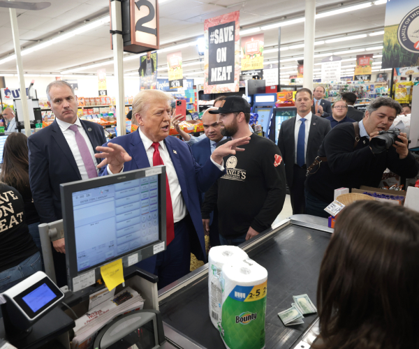 trump gestures with his hands as he stands at a supermarket checkout