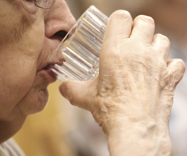 senior citizen takes a pill and a sip of water out of a glass