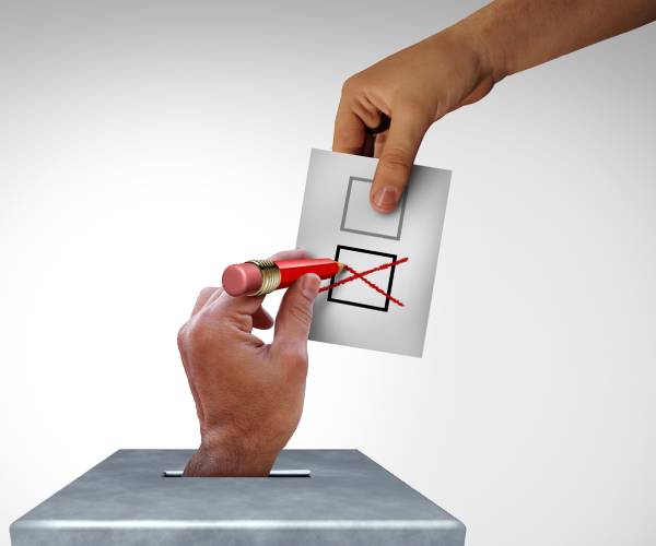 a hand coming up from a voting box and checking the ballot being put into the box