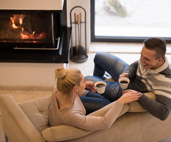 Couple drinking coffee on couch with fire in fireplace