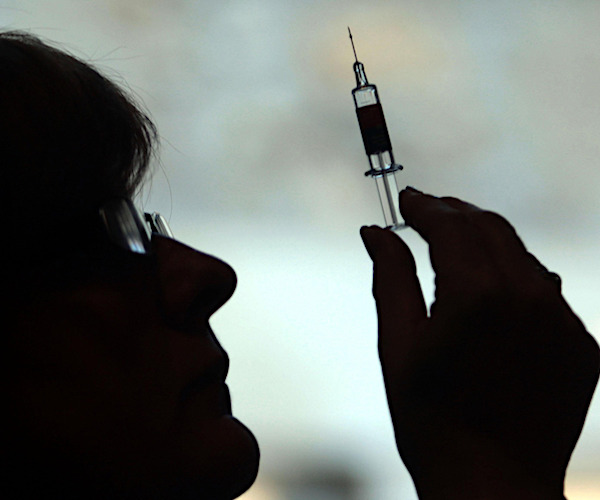 a nurse holds up a syringe and a needle in the foreground shadow