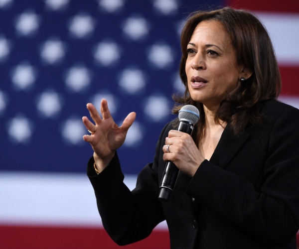 kamala harris speaking with a large american flag hanging behind her