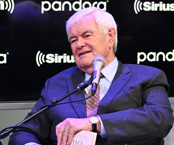 newxt gingrich holds his book and speaks, seated at a mic