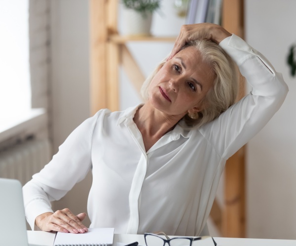 woman at desk working on computer stretching her neck