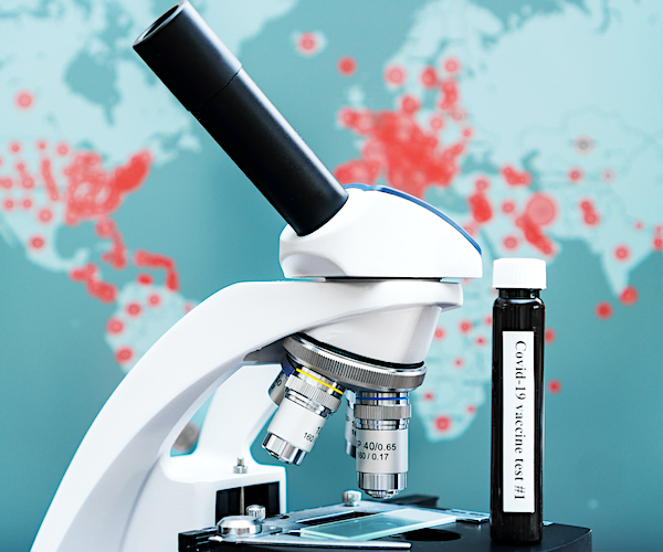 a world coronavirus impact map with a microscope and a vial marked covid-19 vaccine