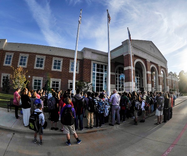 students and adults around a flagpole with heads bowed