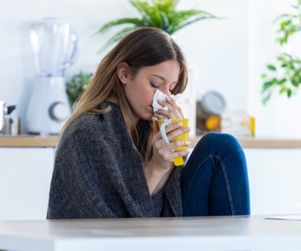 woman not feeling well, with blanket wrapped around and drinking tea