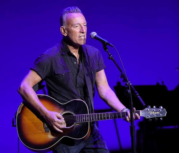 Bruce Springsteen sings into a microphone while playing a guitar