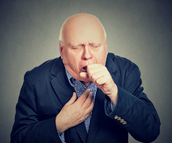 older man in shirt and jacket coughing