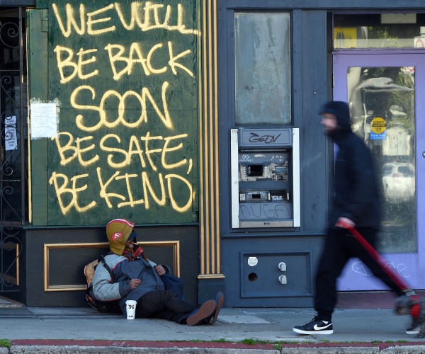 A man walks his dog past a homeless man sleeping under a message painted on a boarded up shop