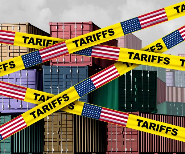 an illustration of shipping containers with yellow tape in front reading tariffs and american flags