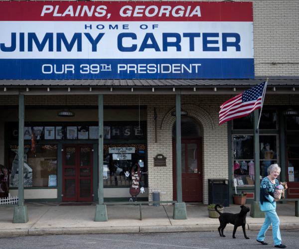 woman and dog walking from building with sign reading plains georgia home of jimmy carter our thirty ninth president