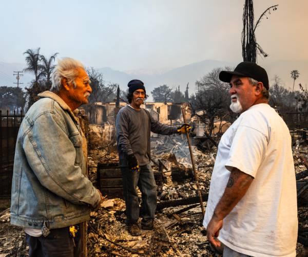 three men standing among the remains of a burned house