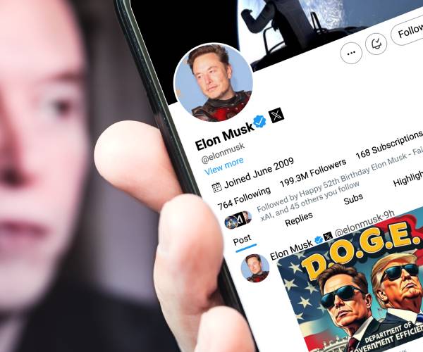 elon musk in the background with a hand holding a phone with musks x account in front with a post about doge