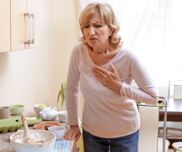 woman in her kitchen with hand on chest in pain