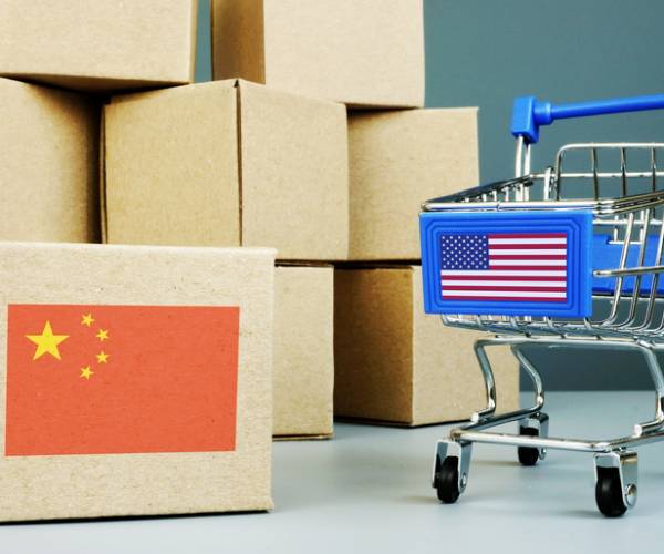 a stack of cardboard boxes with a chinese flag on one next to a shopping cart with an american flag on it