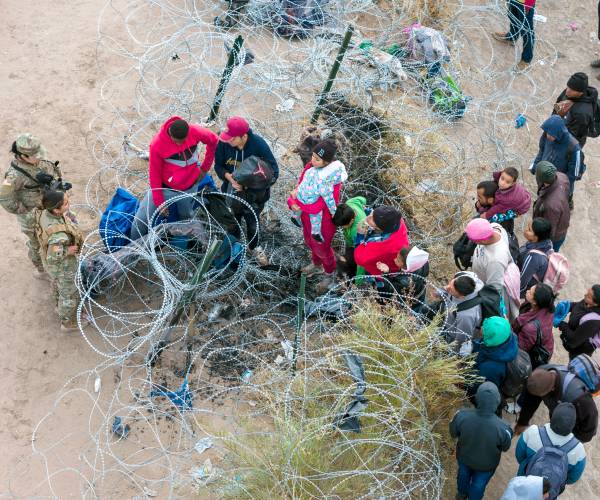 state troops stand in front of migrants trying to walk through razor wire