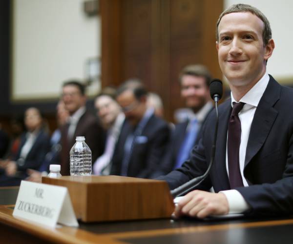 zuckerberg smiling as he sits at a table