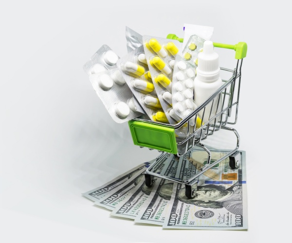 tiny shopping cart with different prescription drugs running over $100 dollar bills