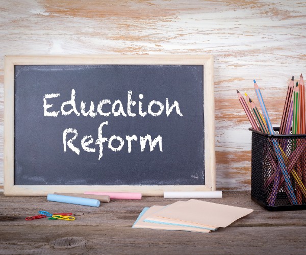 a small blackboard with education reform written on it in chalk with a cup of pencils sitting beside it