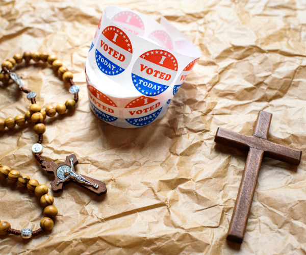 a roll of i voted stickers next to a rosary and a cross