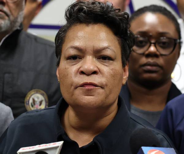 the mayor standing before a microphone at a press conference surrounded by other public officials